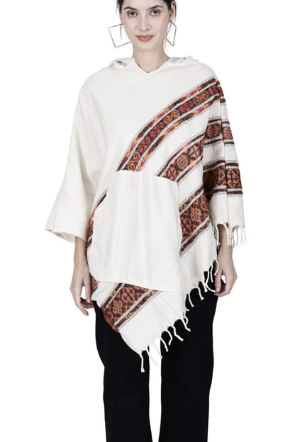 A woman stands facing forward in an aruna kullu handloom "kullu shawl woolen poncho with hood for ladies white 3 patti," featuring red and black geometric patterns and fringed edges, perfect as a party wear poncho.