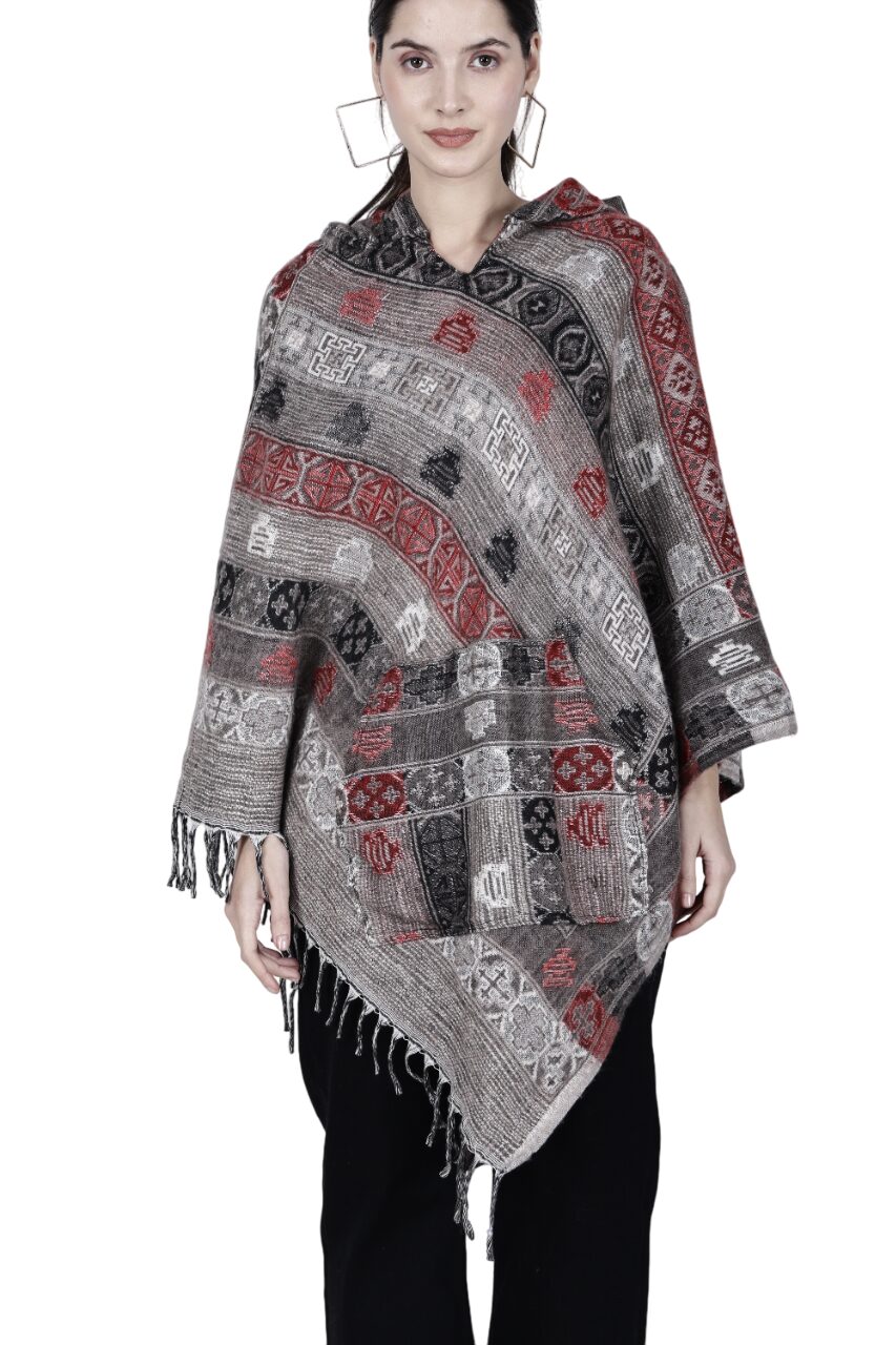 A woman wears the aruna kullu handloom poncho for women, featuring red, black, and gray geometric designs with fringe at the hem, paired with black pants, standing against a white background.