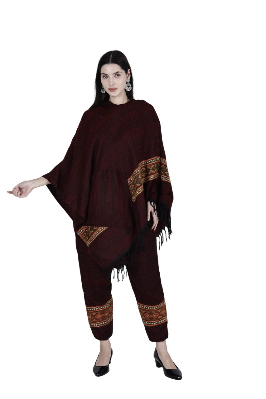 A woman models the "combo pajama and poncho singal patti maroon" by aruna kullu handloom, featuring maroon and black wool with patterned borders and handwoven embroidery, standing against a white background looking at the camera.