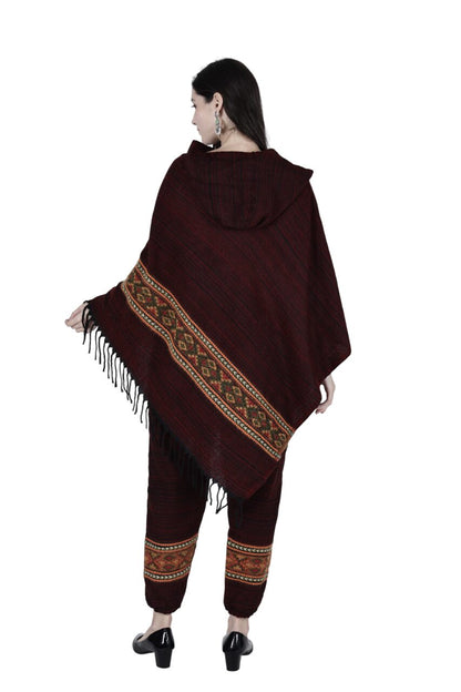 A woman stands facing away, modeling the aruna kullu handloom combo pajama and poncho singal patti maroon set, featuring handwoven embroidery and fringe, with matching patterned pants. She pairs it with black heels and earrings against a white background.
