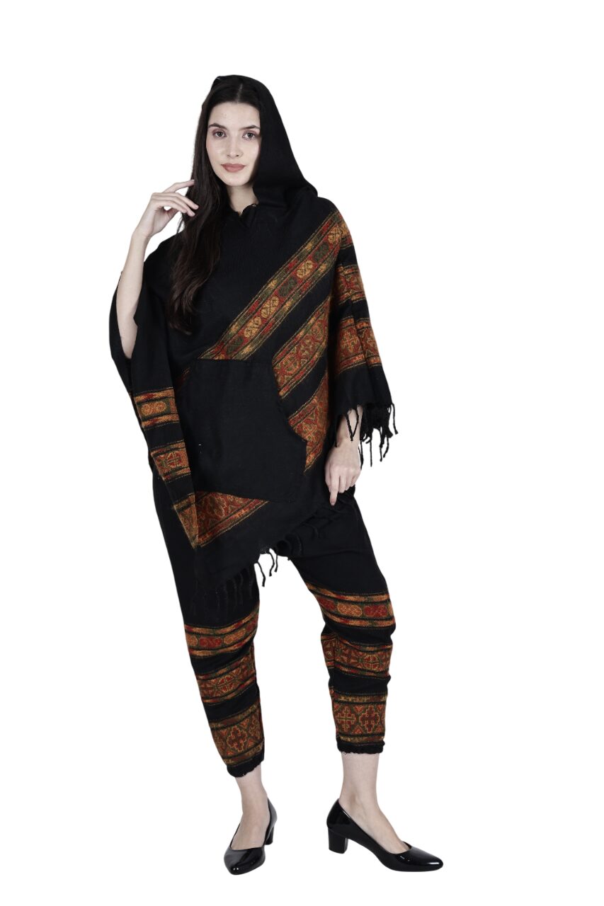 A woman models the aruna kullu handloom kullu shawl combo poncho and pajama black 3 patti, featuring traditional patterns. She stands against a white background, wearing black heels and has long hair with one hand near her face.