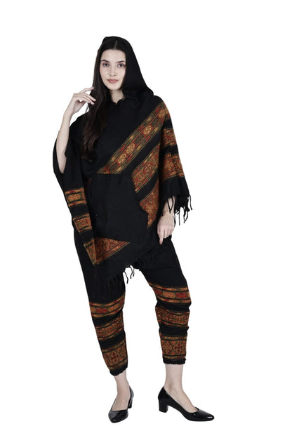 A woman models the aruna kullu handloom kullu shawl combo poncho and pajama black 3 patti, featuring traditional patterns. She stands against a white background, wearing black heels and has long hair with one hand near her face.