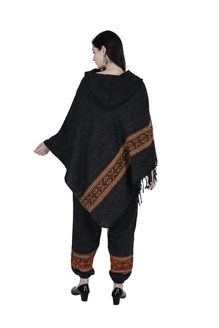 A woman with dark hair models the "combo pajama and poncho black singal patti black" by aruna kullu handloom. She wears earrings and black heeled shoes. The woolen set features handwoven details, shown against a white background.