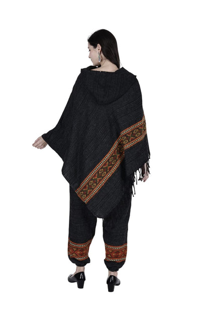 A woman with dark hair models the "combo pajama and poncho black singal patti black" by aruna kullu handloom. She wears earrings and black heeled shoes. The woolen set features handwoven details, shown against a white background.