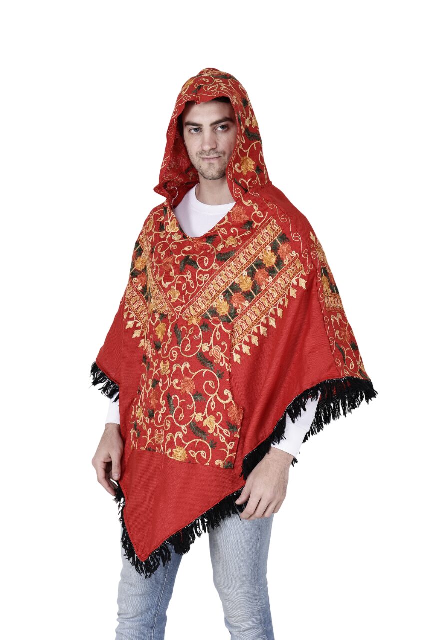 A man wearing the aruna kullu handloom Poncho kashmiri embroidery red, featuring gold and black embroidery with black fringe, stands against a white background.