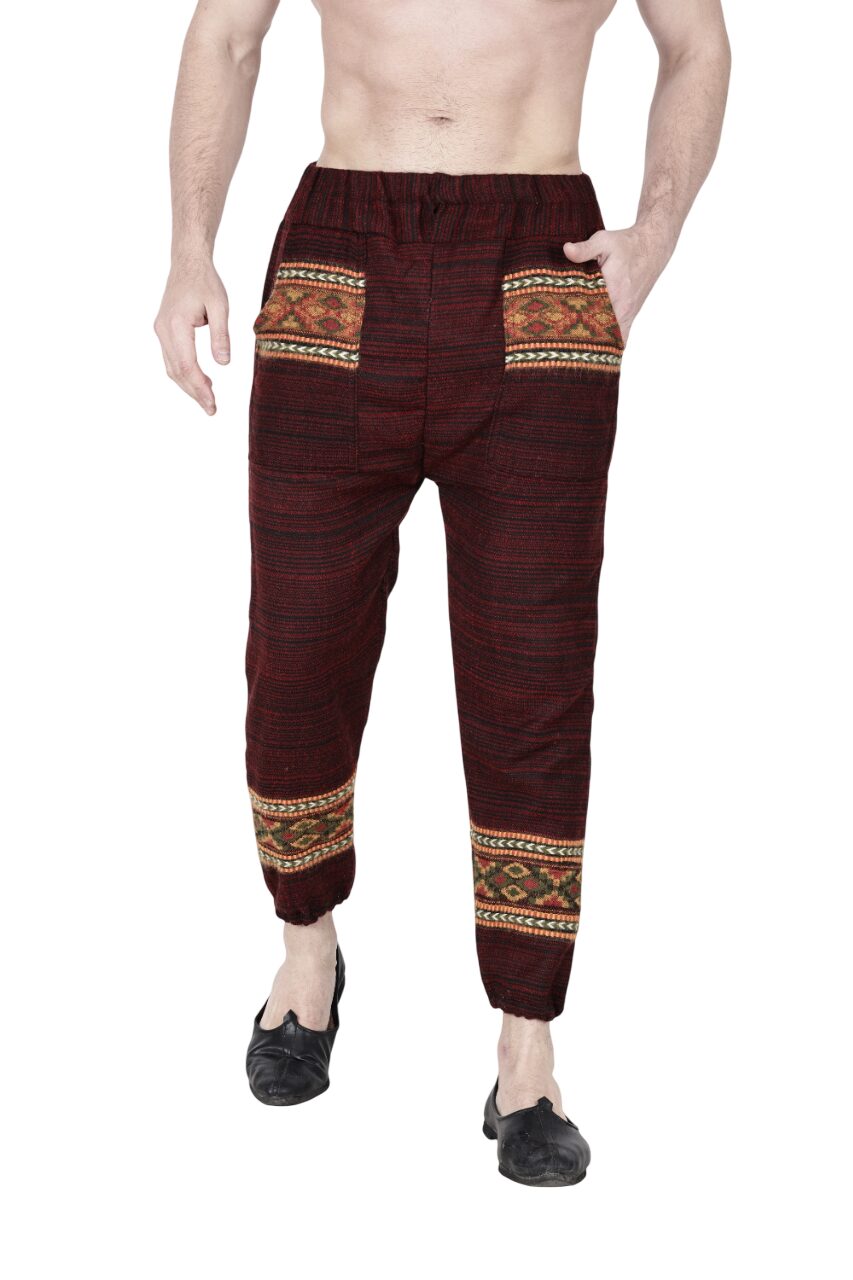 A man models the aruna kullu handloom Pajama for men maroon, featuring colorful patterned pockets and calf bands, standing barefoot with hands in pockets against a white background.