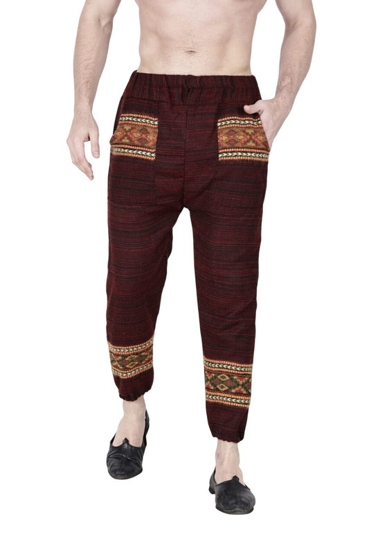 A man models the aruna kullu handloom Pajama for men maroon, featuring colorful patterned pockets and calf bands, standing barefoot with hands in pockets against a white background.