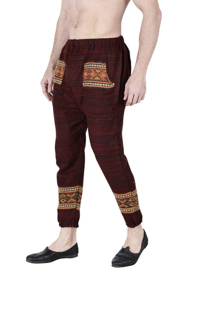 A person models aruna kullu handloom's maroon Pajama for men featuring patterned pockets and ankle bands, barefoot with black slip-ons, against a white background; upper body is partially out of frame.