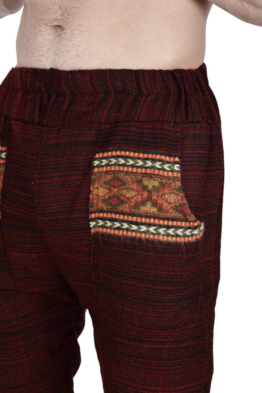 A person models aruna kullu handloom's Pajama for men maroon, featuring red and black patterns and a decorative pocket with yellow, red, and green woven design. The partially visible bare torso highlights these cozy pajama pants.