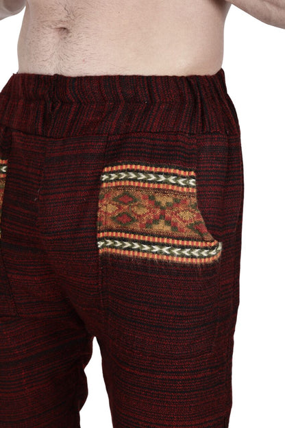 A person models aruna kullu handloom's Pajama for men maroon, featuring red and black patterns and a decorative pocket with yellow, red, and green woven design. The partially visible bare torso highlights these cozy pajama pants.