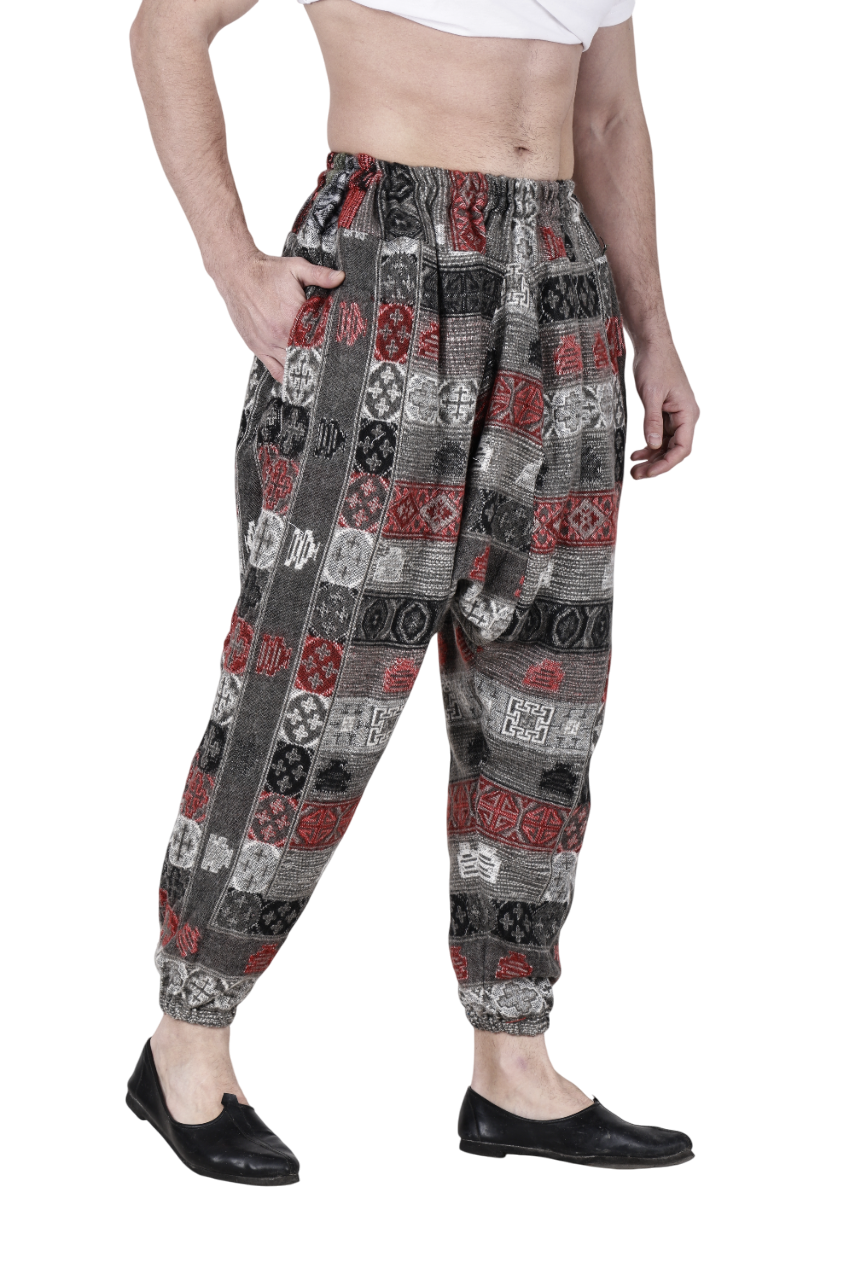 A person wears aruna kullu handloom's Pajama for men loose yoga chess design with red, black, and white geometric patterns, paired with a white cropped top and black slip-ons, posing hand-in-pocket against a white background.