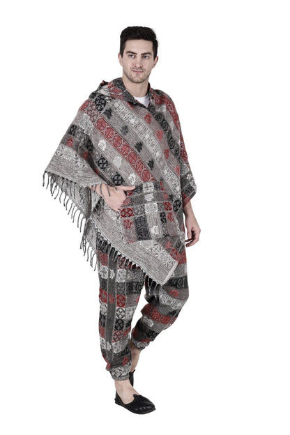 A man stands barefoot against a white background, wearing the Aruna Kullu Handloom Kullu Shawl woolen poncho and pajama combo for men in grey, black, and red with geometric designs.