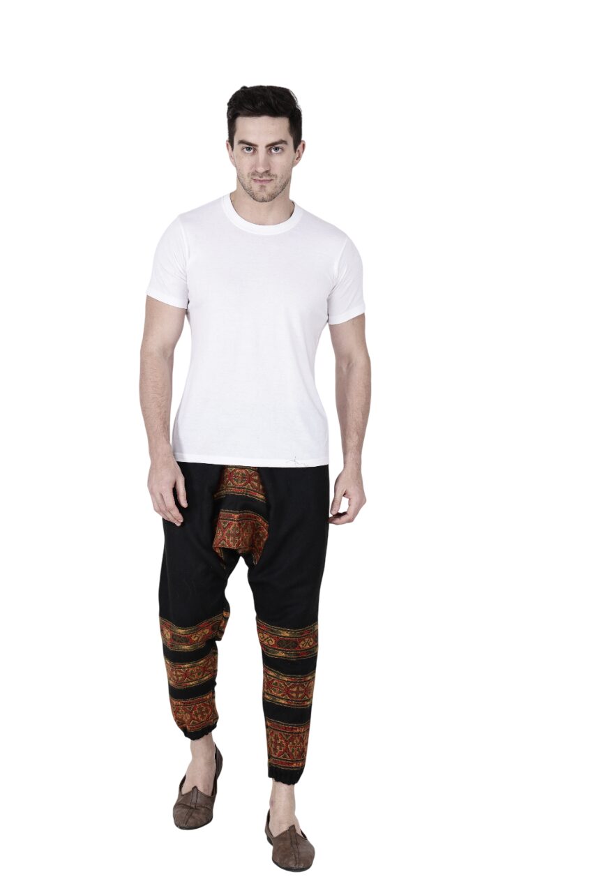 A man wearing a plain white t-shirt, aruna kullu handloom yoga pajama for men loose black 3 patti, and brown slip-on shoes stands against a white background.