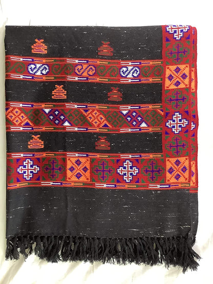 A folded Women’s Yak Wool Kullu Kinnuari Triple Border Shawl in black by aruna kullu handloom showcases colorful geometric and floral patterns with black tassels, displayed on a white background.