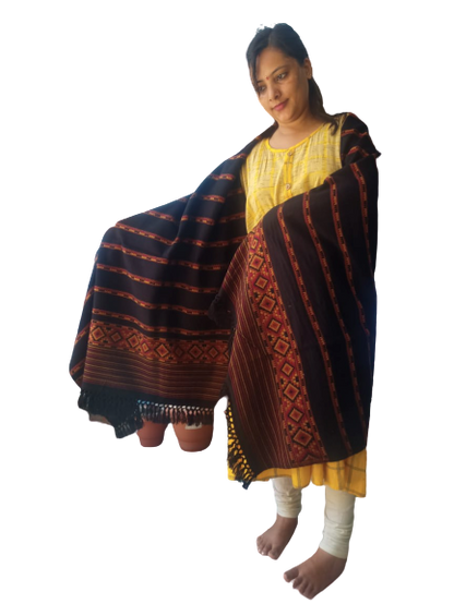 A woman in a yellow kurta and white leggings stands barefoot, draped in the aruna kullu handloom Hand Woven PASHMINA BLACK Shawl—beautifully embroidered for women—against a plain white background.