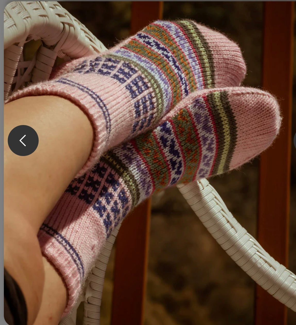 A pair of feet wear aruna kullu handloom Woollen Traditional Hand Made Kullu Socks (Multicolour, Free Size) in pink, resting on a white wicker chair with a softly blurred background.
