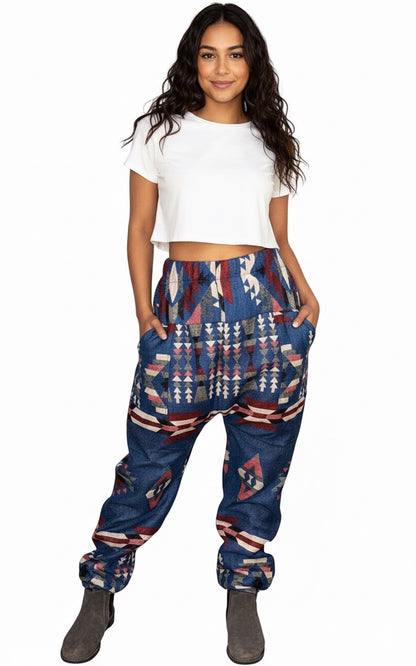 A woman with long wavy hair models the aruna kullu handloom Wool super Soft Warm Pajamas WITH KULLU PATTI WORK in blue, smiling at the camera with her hands in her pockets against a white background.