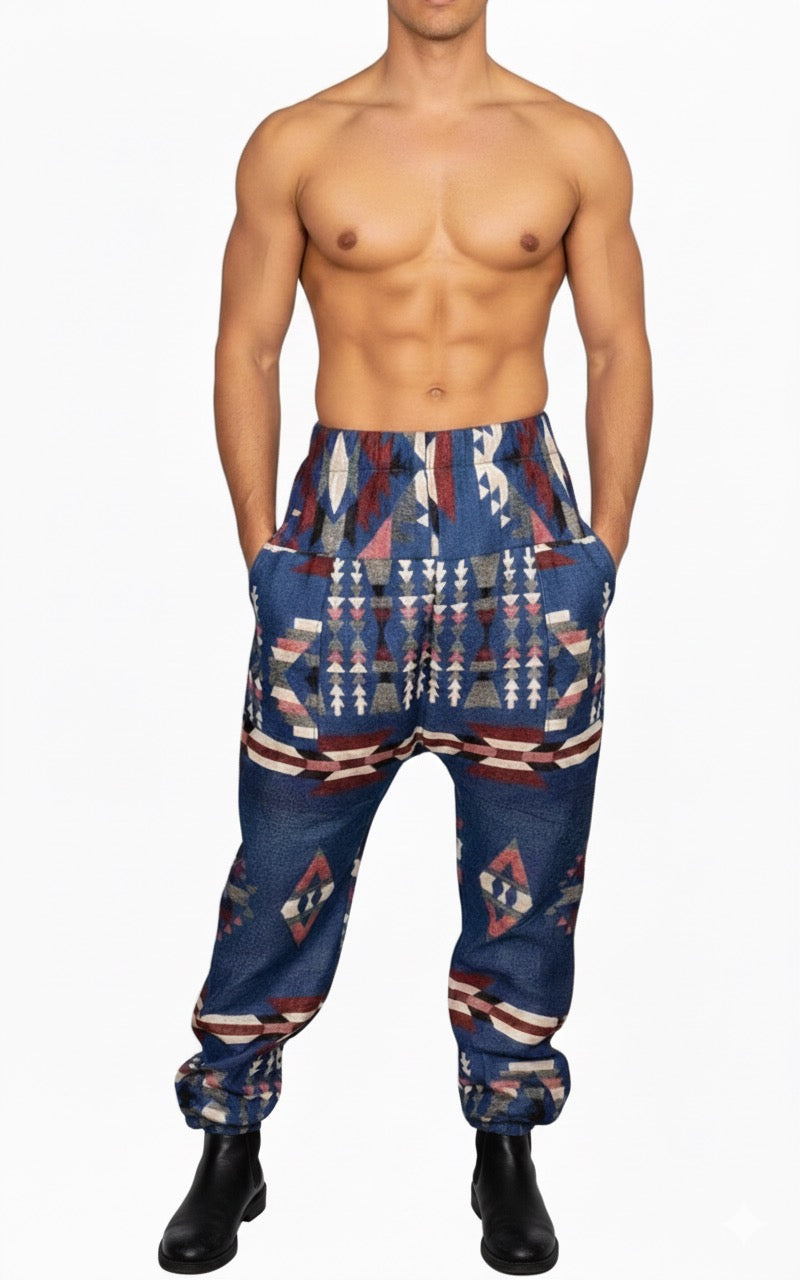 A shirtless man stands against a white background, wearing aruna kullu handloom Wool Super Soft Warm Pajamas WITH KULLU PATTI WORK in blue with a bold multicolored geometric pattern. His hands are casually tucked in his pockets.