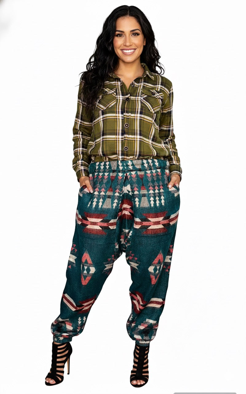A woman smiles with hands in her pockets, wearing aruna kullu handloom’s Wool Super Soft Warm Pajamas WITH KULLU PATTI WORK yoga pajama in green. She has long wavy dark hair and black strappy high-heeled sandals.