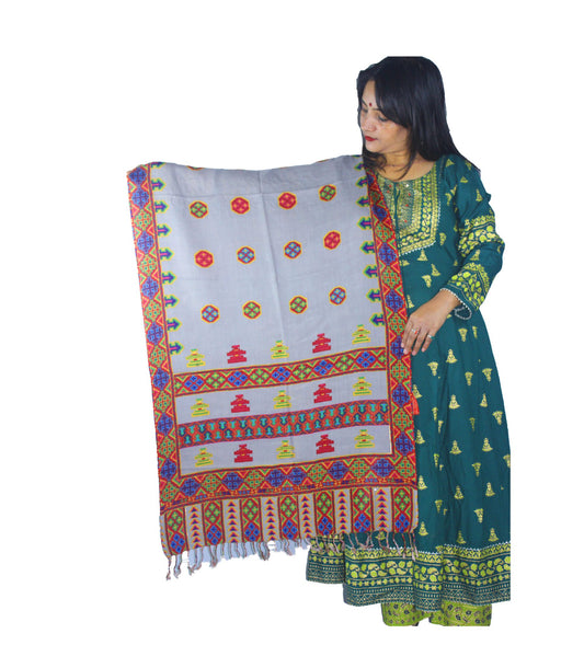 A woman in a green traditional outfit holds up the aruna kullu handloom pure wool stole in grey, featuring beautiful Kullu Kinnauri printed designs. The background is plain white.