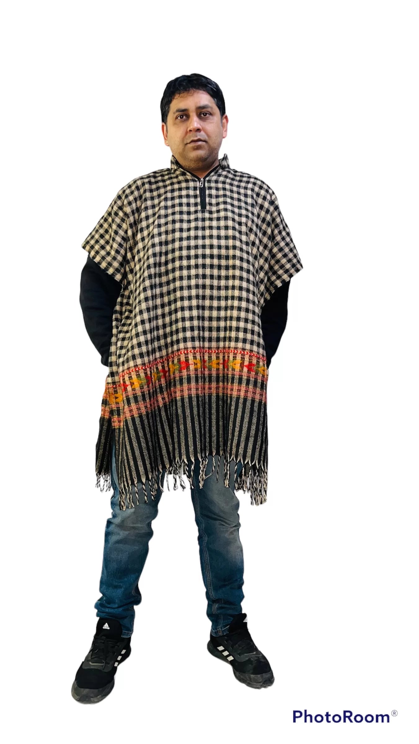 A man stands facing forward, wearing an Aruna Kullu Handloom kullu shawl woolen kaftan for men in black check with red and orange stripes, paired with blue jeans and black sneakers against a white background.