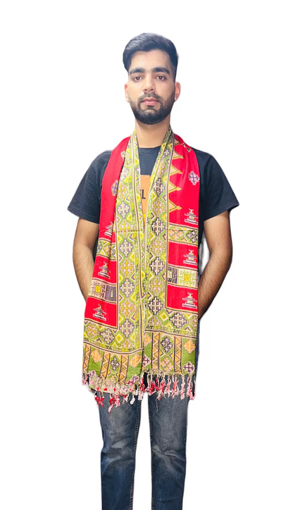 A bearded man stands facing forward, wearing a black t-shirt and jeans, with an aruna kullu handloom kinnauri design muffler red draped over his shoulders against a plain white background—ideal for men’s muffler online shopping.