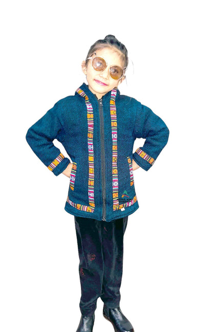 A young girl wearing sunglasses, black pants, and black shoes stands smiling with her hands on her hips, dressed in a blue Woolen Winter Wear ZIPPER HOODIE FOR KIDS with colorful patterned trim against a white background.
