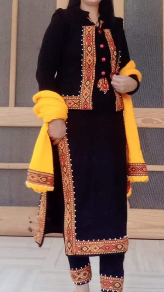 A woman in a traditional black outfit with aruna kullu handloom's KULLU Patti (LACE) Border (3M), matching pants, and Pula Chappal holds a bright yellow shawl over her arms. Her face is partially out of frame.
