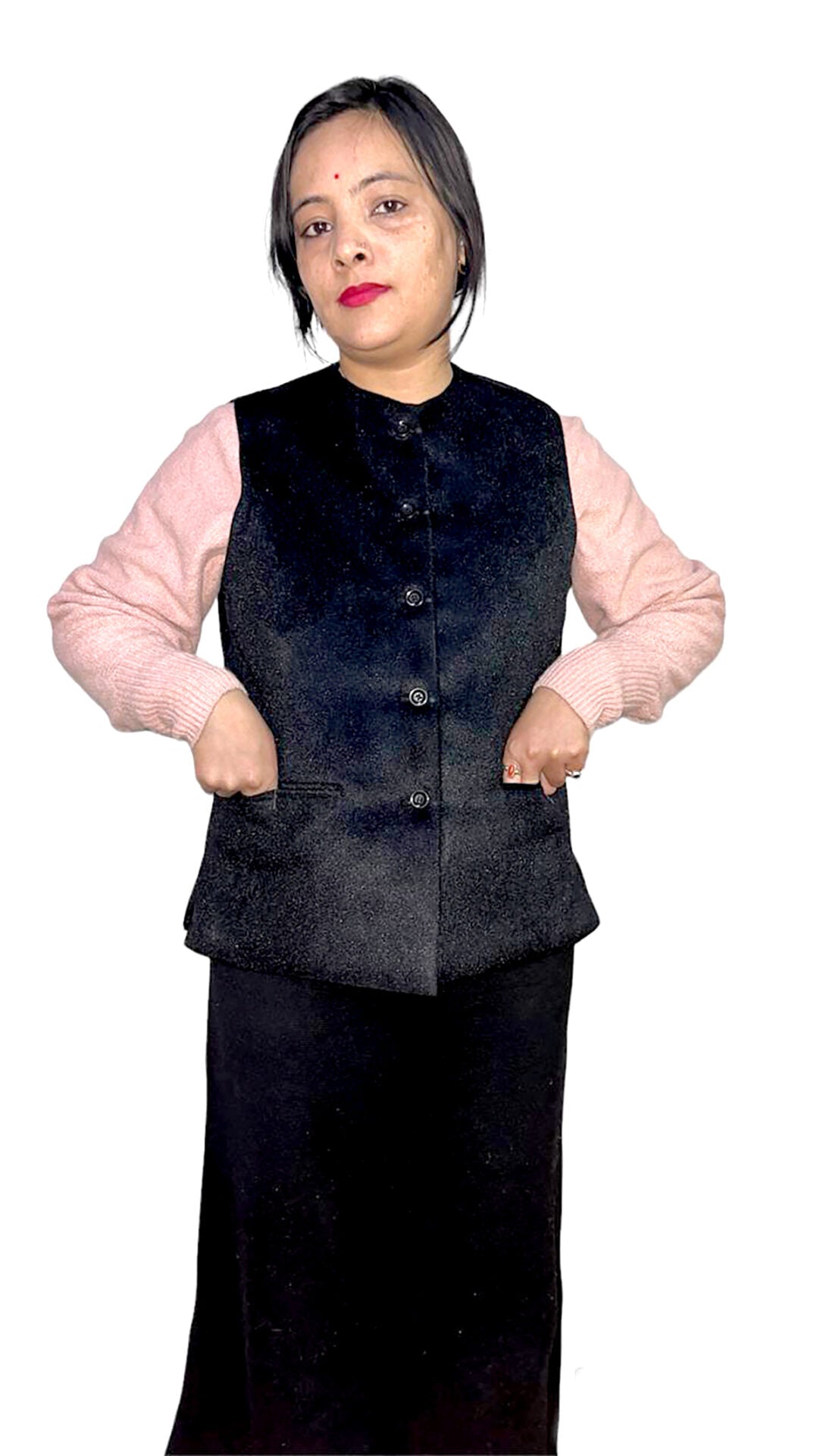 A woman with short dark hair and a red bindi wears the aruna kullu handloom Nehru jacket for women in black over a light pink sweater and long black skirt, standing with her hands in her vest pockets against a white background.
