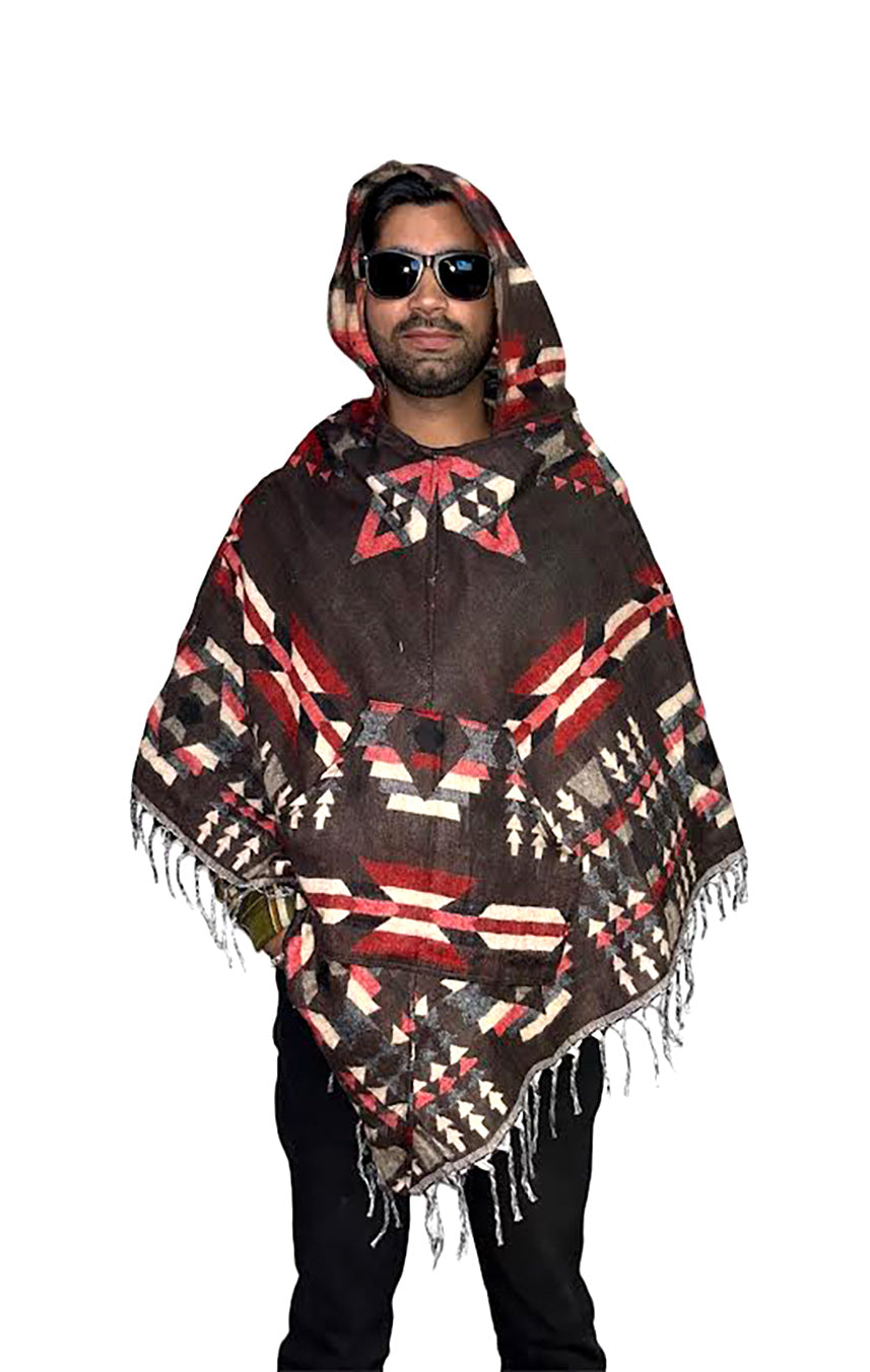 A person in sunglasses wears the Aruna Kullu Handloom kullu shawl woolen poncho with hood in Spanish brown, featuring a red, white, and black geometric pattern and fringed hem, inspired by classic Mexican ponchos.