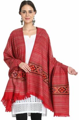 A woman smiles against a white background, draping the red "Kullu Kinnauri Handcrafted Shawl" by aruna kullu handloom over her shoulders, paired with a white kurta, black leggings, and silver earrings. The shawl features elegant fringed edges.