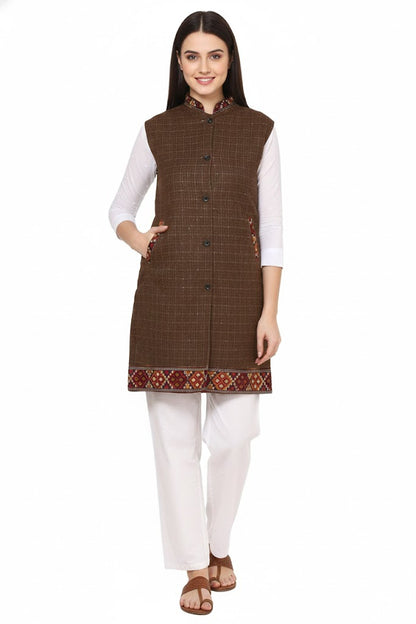 A woman stands smiling against a white background, wearing the aruna kullu handloom Check brown long jacket with kullu lace work over a white kurta and pants.