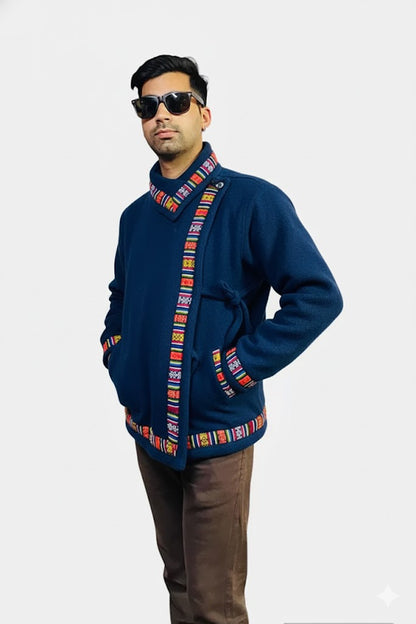 A man wearing sunglasses, brown pants, and an aruna kullu handloom Kullu hoodie Nepali hoodie blue with colorful patterned trim stands with hands in pockets against a plain white background. Kullu hoodie kullu hoodie online wool hoodies kullu lace hoodie kullu patti hoodie