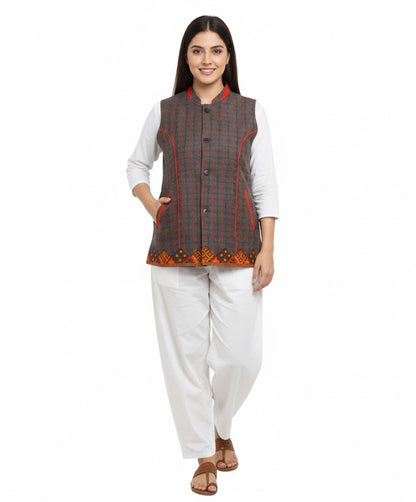 A woman smiles against a white background wearing aruna kullu handloom's woolen winter wear cut design grey checked jacket for women, styled over a white kurta and pants, featuring orange piping and a patterned hem.